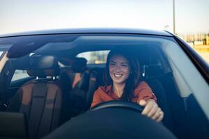 content affaires femme en voyageant avec sa voiture autour le ville. magnifique Jeune content souriant femme conduite sa Nouveau voiture à le coucher du soleil. photo