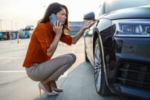 portrait de une désespoir femme accroupi suivant à sa voiture avec plat pneu, problèmes sur le route, dégonflé pneu. photo