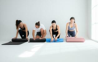 une groupe de femelle et Masculin les athlètes Faire yoga Activités à studio, roulant en haut le yoga tapis photo