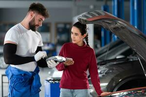 dans un auto réparation boutique, une homme professionnel auto mécanicien slips une femelle client à propos le Coût de voiture réparations et recueille paiement. photo