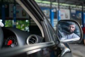 une Jeune homme véhicule technicien travail à l'intérieur une voiture à un auto réparation magasin. photo