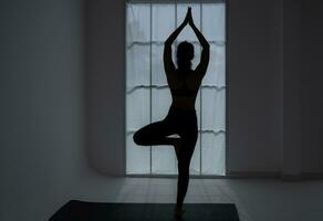 silhouette de une Jeune femme pratiquant yoga dans le chambre. photo