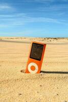 un Orange la musique joueur séance dans le le sable photo