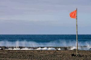 un Orange drapeau sur le plage avec vagues s'écraser dans le Contexte photo