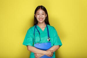 portrait de une magnifique Jeune femme dans une Jaune arrière-plan, asiatique femme portant une médecins uniforme fait du une souriant expression, une Jeune femme portant une médical stéthoscope a une amical expression. photo