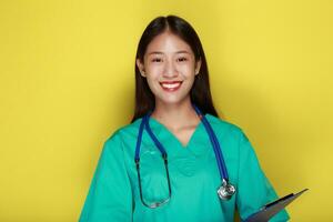 portrait de une magnifique Jeune femme dans une Jaune arrière-plan, asiatique femme portant une médecins uniforme fait du une souriant expression, une Jeune femme portant une médical stéthoscope a une amical expression. photo