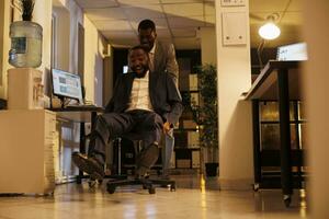 de bonne humeur souriant les hommes d'affaires ayant des sports course compétition dans moderne Commencez bureau, prise Pause de travail et ayant amusement. espiègle les hommes d'affaires dans formel costume profiter équitation bureau chaise photo