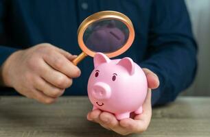 une homme regards à une porcin banque avec une grossissant verre. enquêter Capitale origines. anti argent blanchissage, impôt évasion. transparence et responsabilité. étude termes et conditions sur dépôt. photo