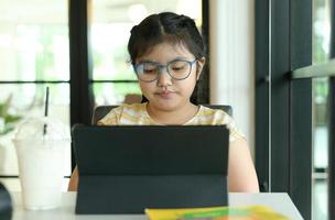 une fille portant des lunettes étudie en ligne avec une tablette.