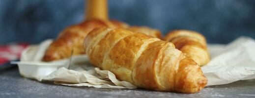 une pile de délicieux Frais des croissants servi avec beurre. sur une gris table avec une bleu Contexte. photo