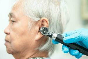 audiologiste ou ent médecin utilisation otoscope vérification oreille de asiatique Sénior femme patient traiter audition perte problème. photo