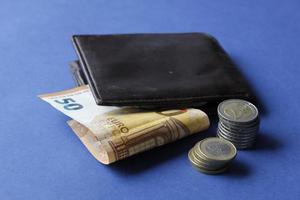 billet de cinquante euros, pièces empilées et portefeuille en cuir marron sur fond bleu photo