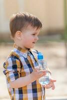 Beau garçon les boissons clair l'eau de une bouteille sur une ensoleillé journée à l'extérieur photo