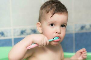 charmant bébé brossage le sien les dents avec une brosse à dents dans le salle de bains photo