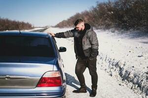 homme des stands près le sien cassé voiture dans hiver photo