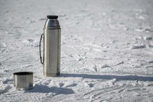 le thermos des stands sur la glace avec une tasse de chaud thé photo