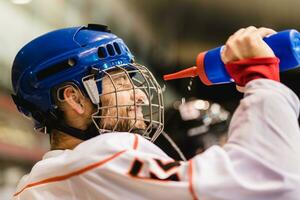 le hockey joueur les boissons de une bouteille et puis verse l'eau plus de le sien visage photo