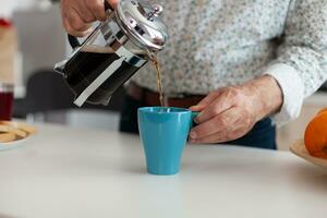 Sénior homme effusion chaud boisson après en train de préparer café en utilisant français presse dans cuisine pour petit déjeuner. personnes âgées la personne dans le Matin profiter Frais marron café Expresso tasse caféine de ancien agresser photo