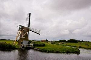 une Moulin à vent est suivant à une rivière dans une champ photo