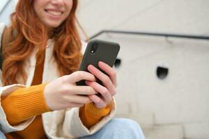 proche en haut portrait de les filles mains en portant téléphone intelligent. femme est assis sur escaliers sur rue et les usages mobile téléphone, chats, lit message ou les usages application photo