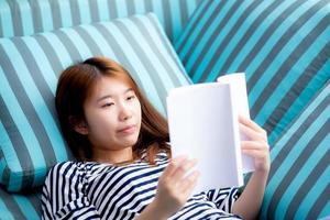 jeune femme asiatique se détendre allongé livre de lecture sur le canapé. photo