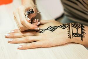 artiste appliquant henné tatouage sur femmes mains. mehndi est traditionnel Indien décoratif art. fermer photo