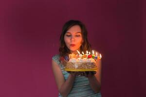 portrait de jolie fille en portant anniversaire gâteau et soufflant bougies à fête photo