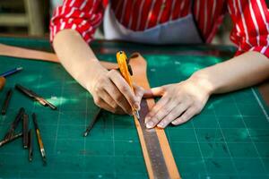 fermer et surgir mains de cuir fabricant en utilisant une coupeur couteau à Couper une pièce de cuir feuille selon à le conception à apporter en dehors à Coudre dans des produits pour clients. photo