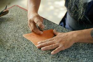 fermer main de cuir artisan est soigneusement à faire une cuir produit pour une client., cuir artisan concept. photo