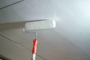 fermer une peint rouleau est peint blanc sur le plafond de le maison. photo