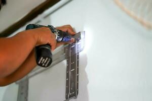 fermer mains de constructeur en portant un électrique percer est forage une trou dans le mur pour installer air état à construction placer. photo