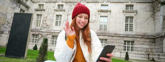 souriant Jeune femme dit Bonjour sur vidéo discuter, connecte Publique Wifi dans parc et pourparlers Quelqu'un en ligne avec téléphone intelligent app photo