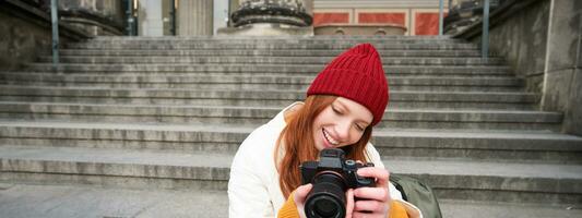 portrait de Jeune photographe fille, est assis sur escaliers avec professionnel caméra, prend Photos en plein air, fabrication mode de vie tournage