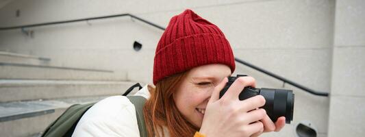 Urbain gens et mode de vie. content roux femme prend Photos, en portant professionnel numérique caméra, photographier sur des rues photo