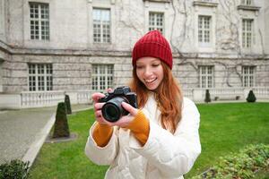 content roux fille touristique, prend Photos, photographe avec professionnel caméra des promenades autour ville et capture magnifique des photos