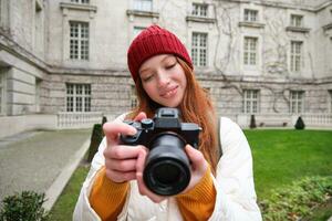 content roux fille touristique, prend Photos, photographe avec professionnel caméra des promenades autour ville et capture magnifique des photos