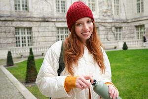 portrait de content fille voyageur, en buvant chaud thé de thermos tandis que en marchant et explorant ville. touristique avec ballon souriant à caméra photo