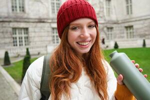 portrait de content fille voyageur, en buvant chaud thé de thermos tandis que en marchant et explorant ville. touristique avec ballon souriant à caméra photo