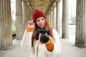 Jeune roux femelle photographe, fait du mode de vie tournage dans ville centre, prend Photos et sourires, regards pour parfait tir, fait du image