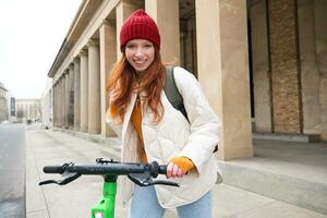 souriant roux européen fille disques Publique scooter, touristique explore ville, monte dans ville centre photo