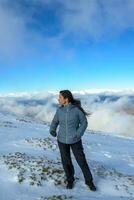 âge moyen latina femme sur une enneigé Montagne au dessus le des nuages photo