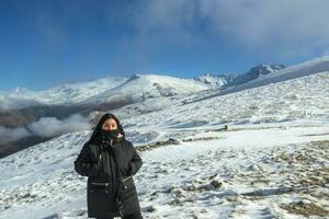 Jeune latina femme posant avec noir veste sur neigeux Montagne très content, gratuit, complet, positif, prendre plaisir vie. photo