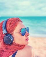 cool femme écoute à la musique sur le plage. le fille jouit une magnifique vue de le mer et écoute à musique. photo