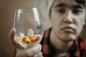 triste gars en portant une verre de pilules et drogues. photo