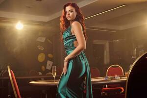 Jeune magnifique femme est posant contre une poker table dans luxe casino. photo