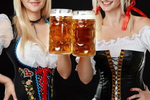 Jeune et magnifique bavarois les filles avec deux Bière des tasses sur noir Contexte photo