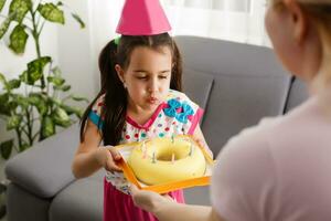 les enfants virtuel anniversaire fête avec gâteau en ligne ensemble avec sa ami dans vidéo conférence. avec numérique Téléphone pour une en ligne réunion. fille célébrer anniversaire en ligne dans quarantaine temps photo