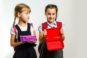 élèves de primaire école avec boîtes à lunch dans mains. les filles avec sacs à dos sont en mangeant fruit. début de cours. premier journée de automne. photo