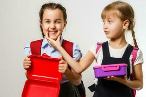 élèves de primaire école avec boîtes à lunch dans mains. les filles avec sacs à dos sont en mangeant fruit. début de cours. premier journée de automne. photo