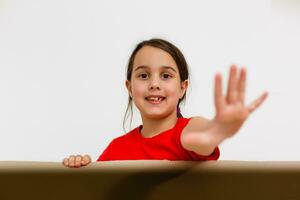 une de bonne humeur enfant est assis à l'intérieur une courrier boîte. le tête de une peu fille coups d'oeil en dehors de une corton boîte. le bébé arrivée dans une Nouveau maison dans une postal colis. portrait de une enfant avec bleu yeux. photo